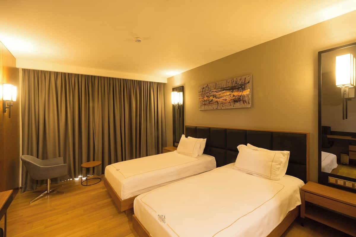 Ein Hotelzimmer mit zwei Betten, einem Schreibtisch, einem Stuhl, einem kleinen Tisch, einem Bild an der Wand und einem Spiegel.