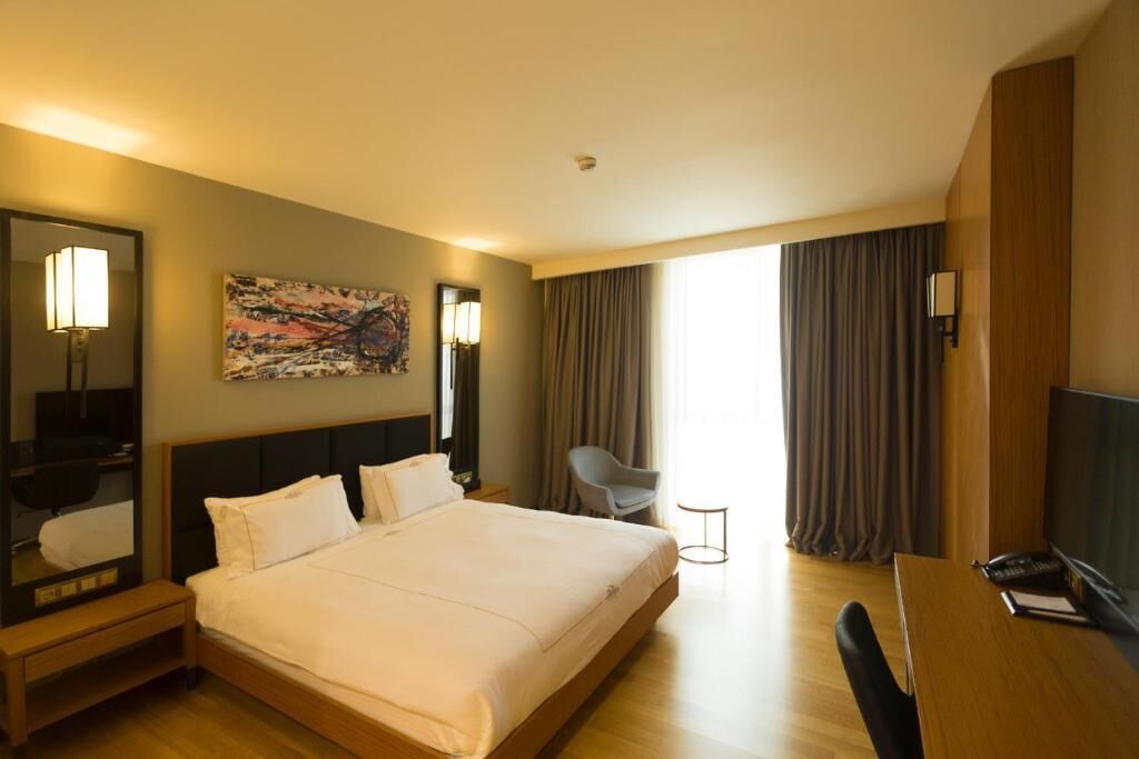 A hotel room with a large bed, a desk, a chair, a mirror, and a painting on the wall.