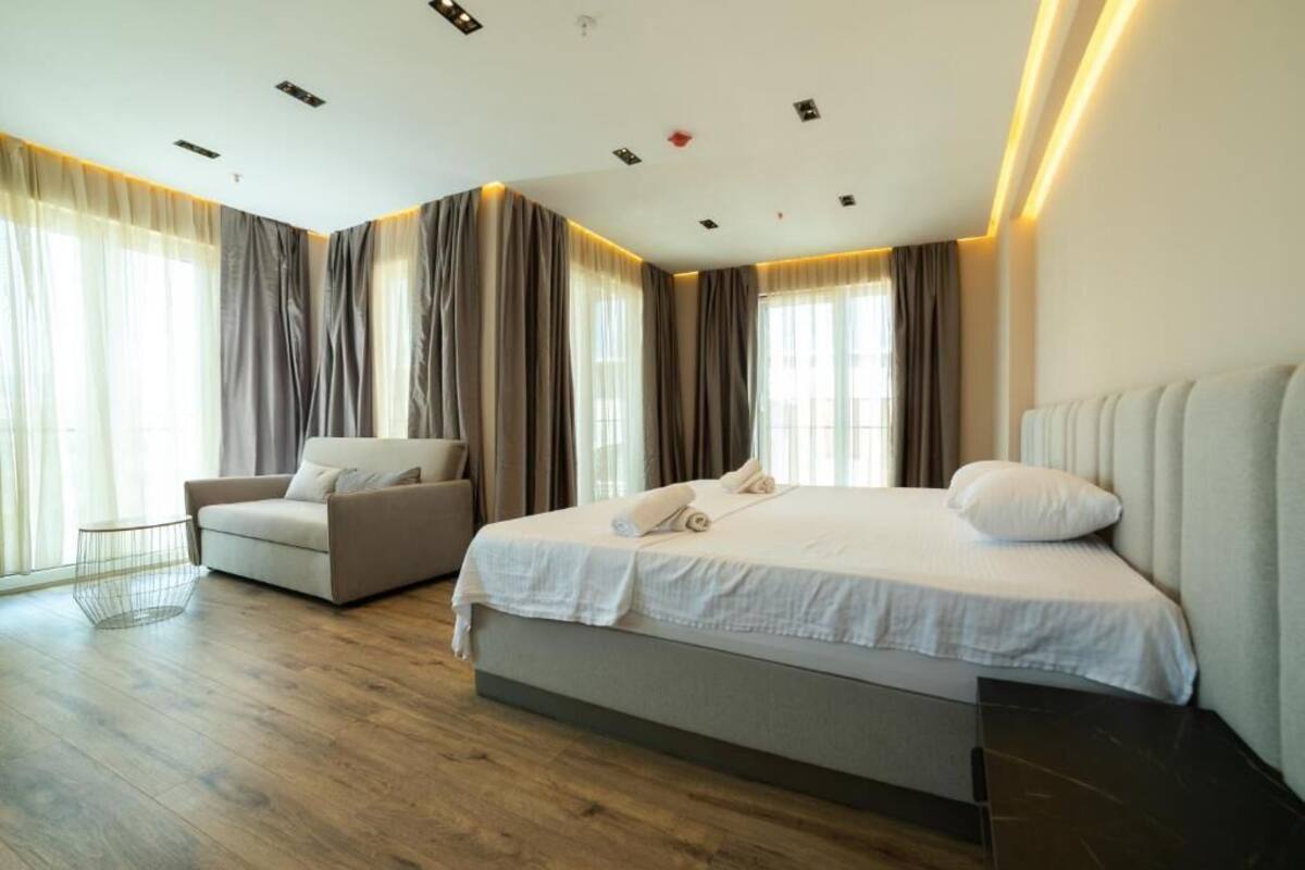 A modern hotel room with a large bed, a sofa, and a window with curtains.