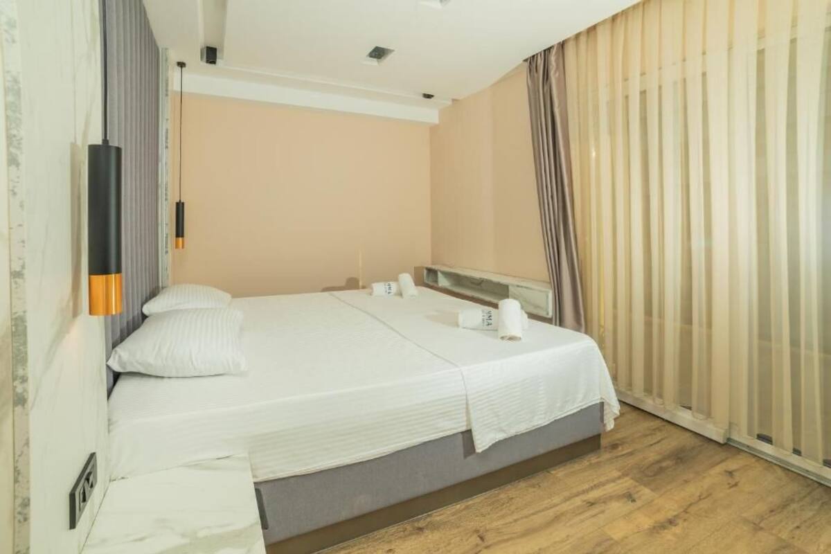 A hotel room with a bed, a mirror, a window with curtains, and a wooden floor.