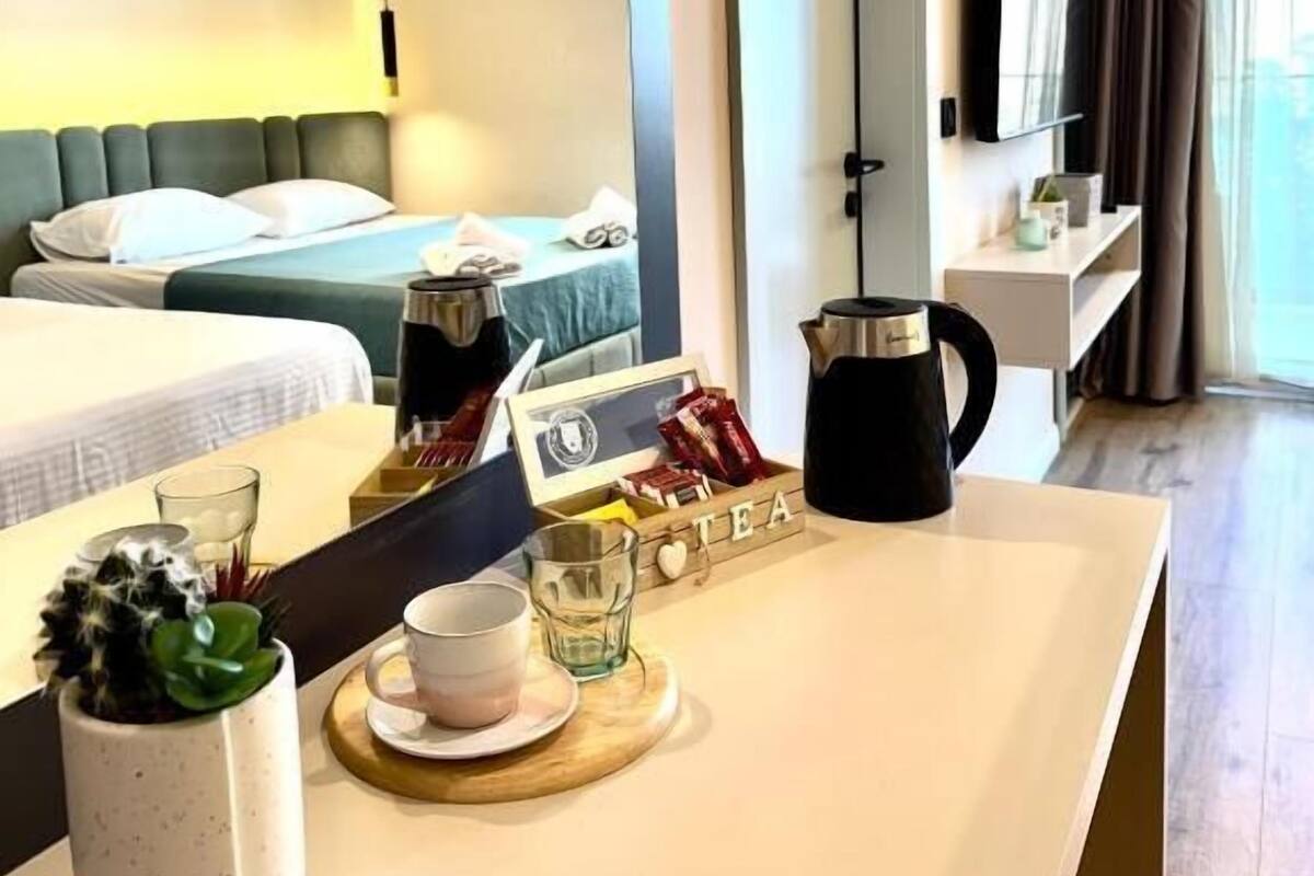 A hotel room with a bed, a bedside table with a kettle, a cup, and a tray with tea bags.