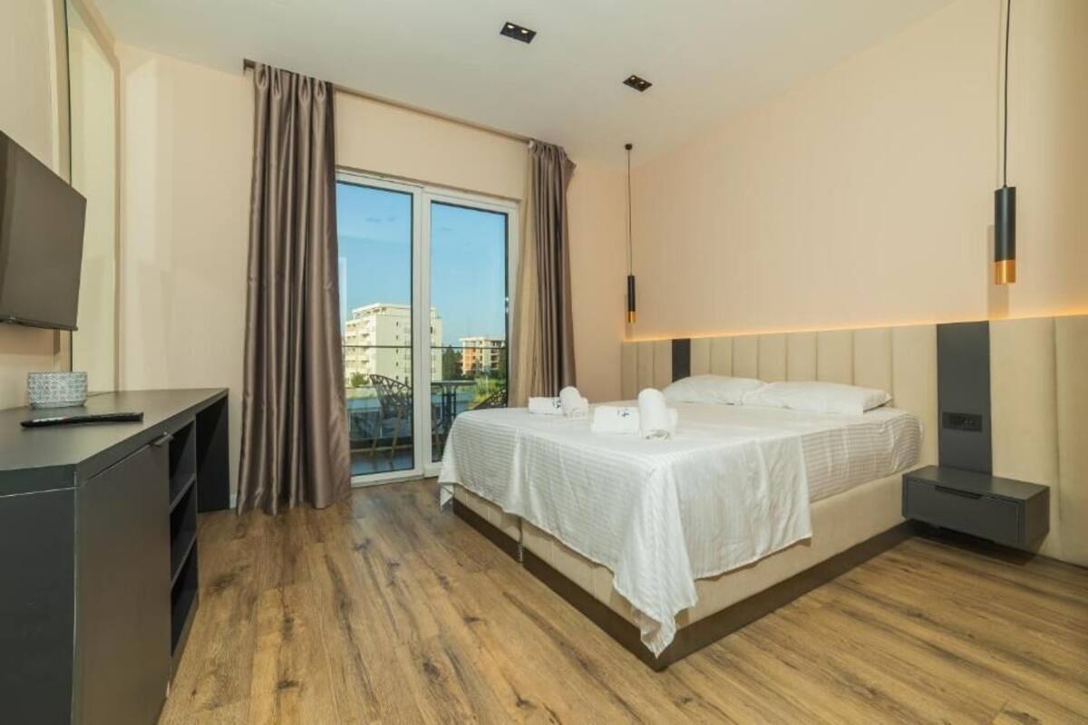 A hotel room with a bed, a desk, a television, and a view of buildings through a glass door.