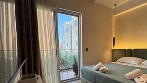 Et moderne soveværelse med seng, et lille bord med plante, et vindue med gardiner og en balkon.