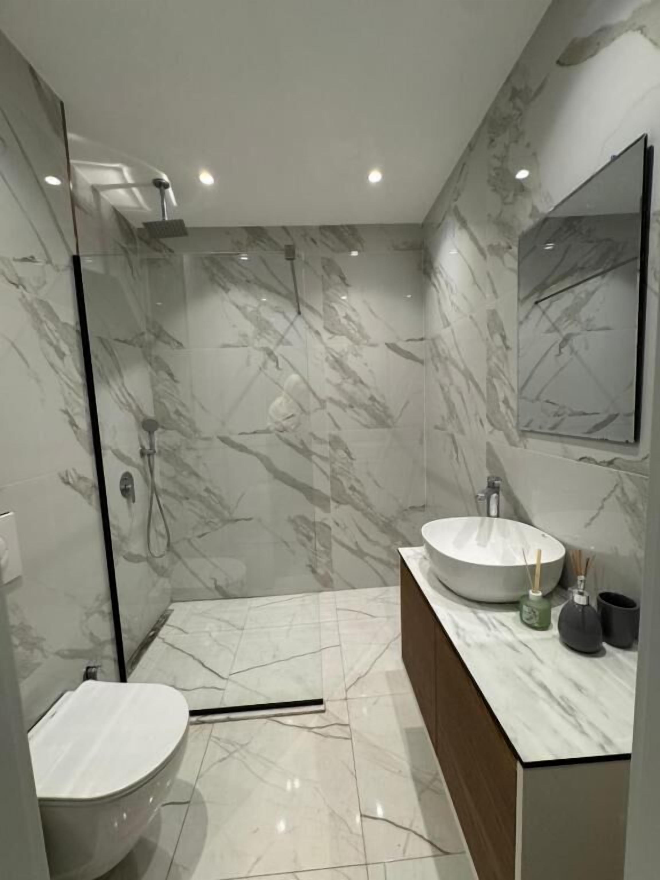 Un baño moderno con ducha de vidrio, lavabo redondo y un inodoro.