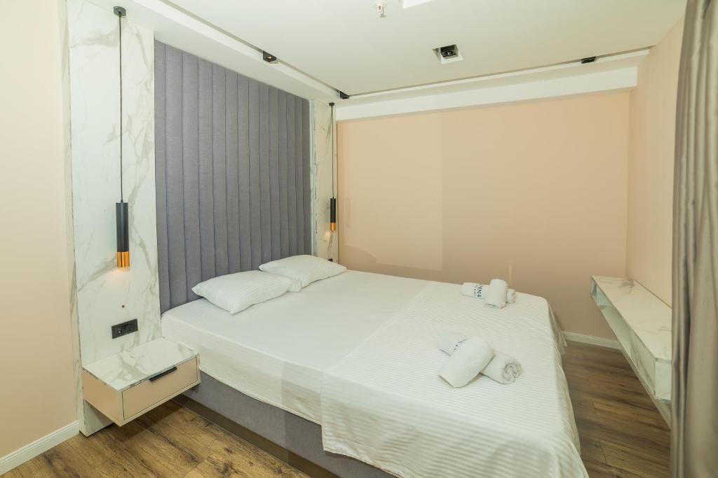 A modern hotel room with a bed, bedside table, and a built-in shelf.