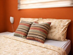 Ein Bett mit floralem Bettzeug, zwei gestreifte Kissen und ein an der Wand befestigtes Telefon.