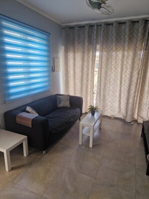 Ein Wohnzimmer mit einer Couch, einem kleinen Tisch und einem Fenster mit Jalousien.