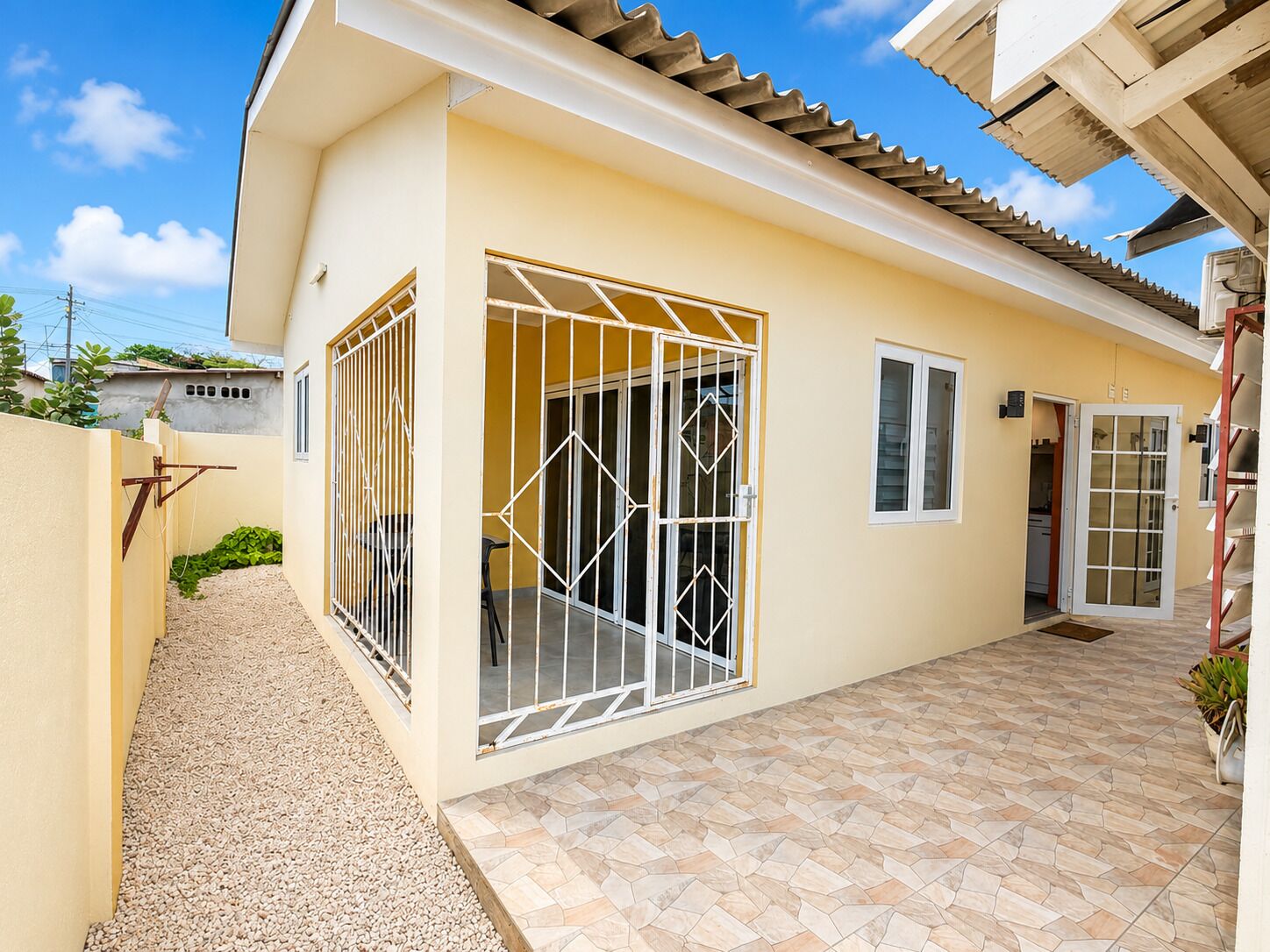 A residential building with a gated entrance, a tiled patio, and a door leading to an interior space.
