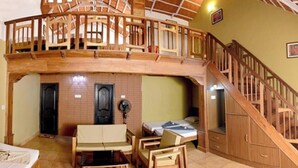 A room with a lofted sleeping area, a wooden staircase, a fan, and a bed with a white comforter. - Upasana Retreat (Mudigere)