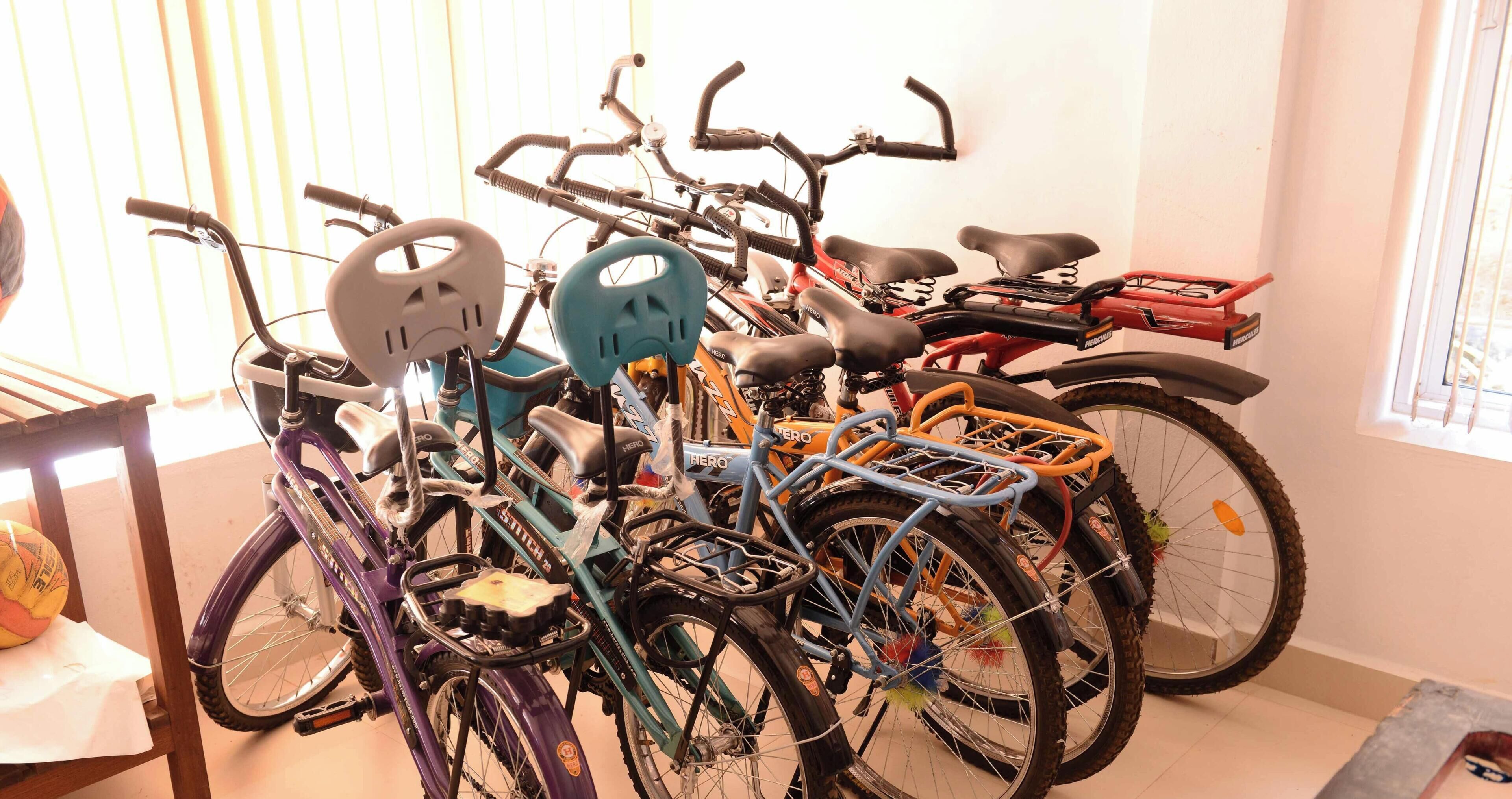 A collection of bicycles with various accessories, including helmets and baskets, arranged in a room with a window.