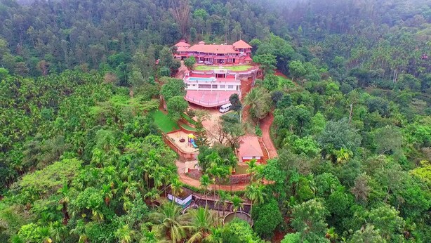 A large, multi-story building with a red roof, surrounded by dense forest. - Upasana Retreat (Mudigere)