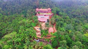 Un edifici gran de diverses plantes amb un teulat vermell, envoltat de bosc dens.