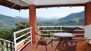 A balcony with wicker furniture and a view of green hills. - Upasana Retreat (Mudigere)