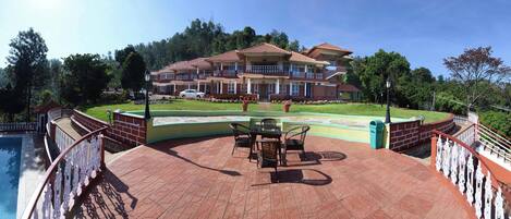 A large house with a swimming pool, a covered patio area, and a view of the surrounding forest.