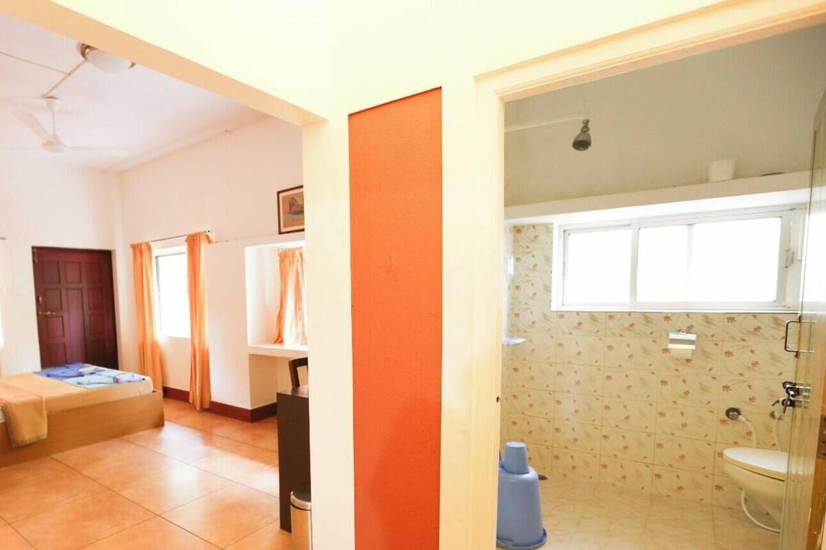 Ein Zimmer mit Bett, Schreibtisch, Stuhl, einem Fenster mit Vorhängen sowie einem Badezimmer mit Toilette und Dusche.