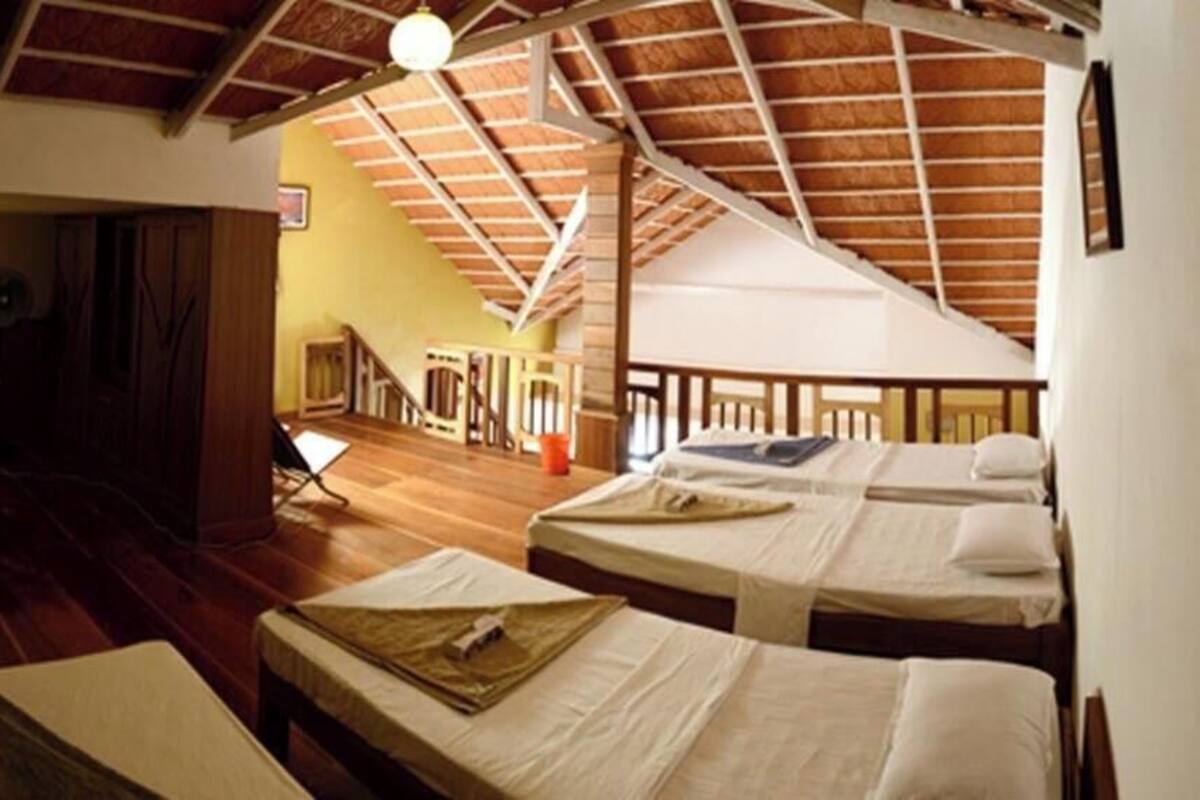 Ein Zimmer mit zwei Betten, einem kleinen Tisch, einem Ventilator und einer Treppe zu einer oberen Ebene.
