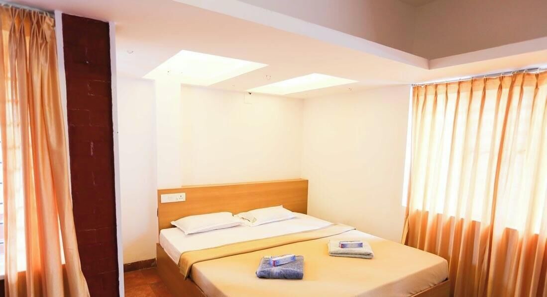 Una cama individual con cabecera de madera, una mesita de noche pequeña y una ventana con cortinas.