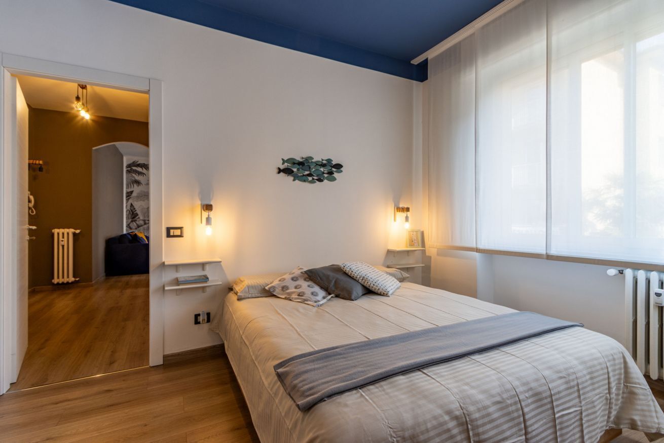 Une chambre à coucher avec un lit, des lampes de chevet, un élément de décoration murale et une fenêtre avec des rideaux.