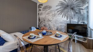 A modern room with a round dining table, clear chairs, a sofa, a TV, and a wall mural. - Casa Giada - Downtown Arona - 500 m from the lake - WiFi - By Guestaly (Arona)