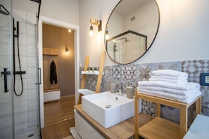 A modern bathroom with a large mirror, a white sink, and a wooden vanity with towels.