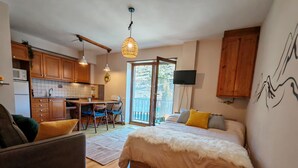 Ein Schlafzimmer mit Bett, einer Couch, einem Esstisch mit Stühlen, einer Küchenzeile und einem Balkon mit Blick.