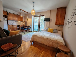 Un dormitorio con cama, sofá, mesa de comedor con sillas, zona de cocina y balcón con vistas.