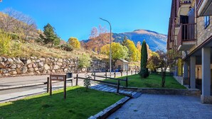 Ein Hotelaufgang mit einer Steinmauer, einer Rasenfläche, einem Holzzaun und einem Berg im Hintergrund.