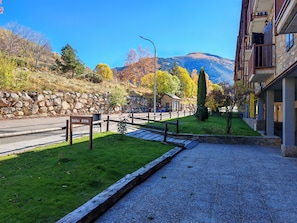 Entrada de hotel con un muro de piedra, área con césped, cerca de madera y una montaña al fondo.