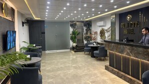 Zona de recepción de un hotel con suelo de mármol, asientos, un mostrador de recepción y una pantalla de televisión.