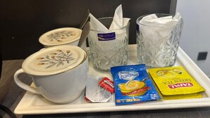 Una bandeja con una taza de café, dos vasos de agua, una toallita, una bolsita de té y un paquete de aperitivos.