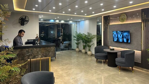 Zona de recepción de hotel con mostrador, área de asientos y pantalla de televisión.