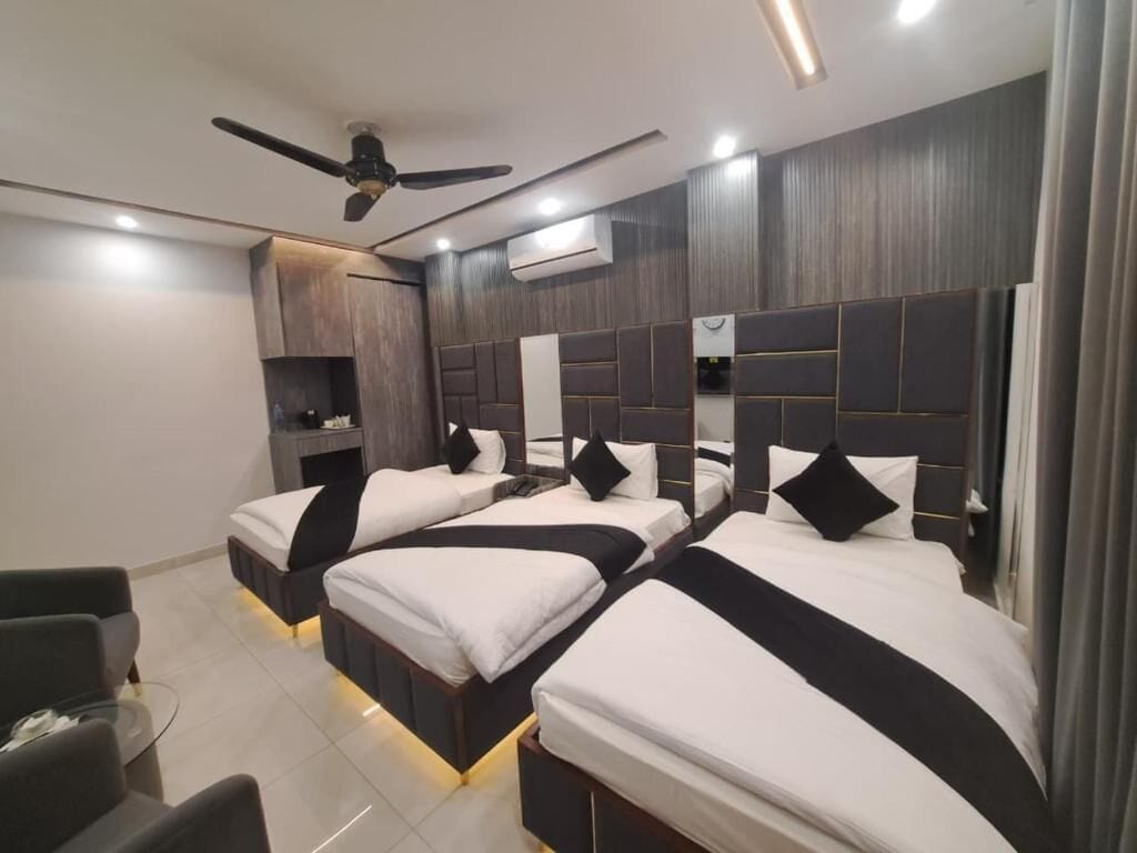 A hotel room with three beds, a ceiling fan, an air conditioning unit, and a small seating area with a table and chairs.