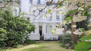 A white building with a garden in front, a staircase leading to the entrance, and outdoor furniture. - South Kensington Garden Escape, by Veeve (London)