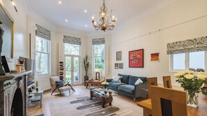 A spacious living room with a fireplace, a chandelier, a sofa, a coffee table, and a dining table with chairs. - South Kensington Garden Escape, by Veeve (London)