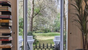 A view through a door with a bookshelf, a black metal gate, and a garden with trees and grass. - South Kensington Garden Escape, by Veeve (London)
