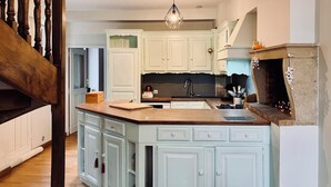 Una cucina con mobili bianchi, un'isola in legno, un camino in pietra e una scala in legno.