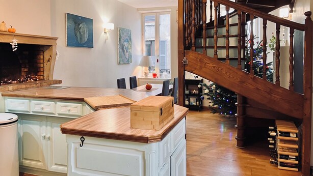 Una cucina con isola in legno, mobili bianchi, un caminetto e una scala che conduce a una sala da pranzo.