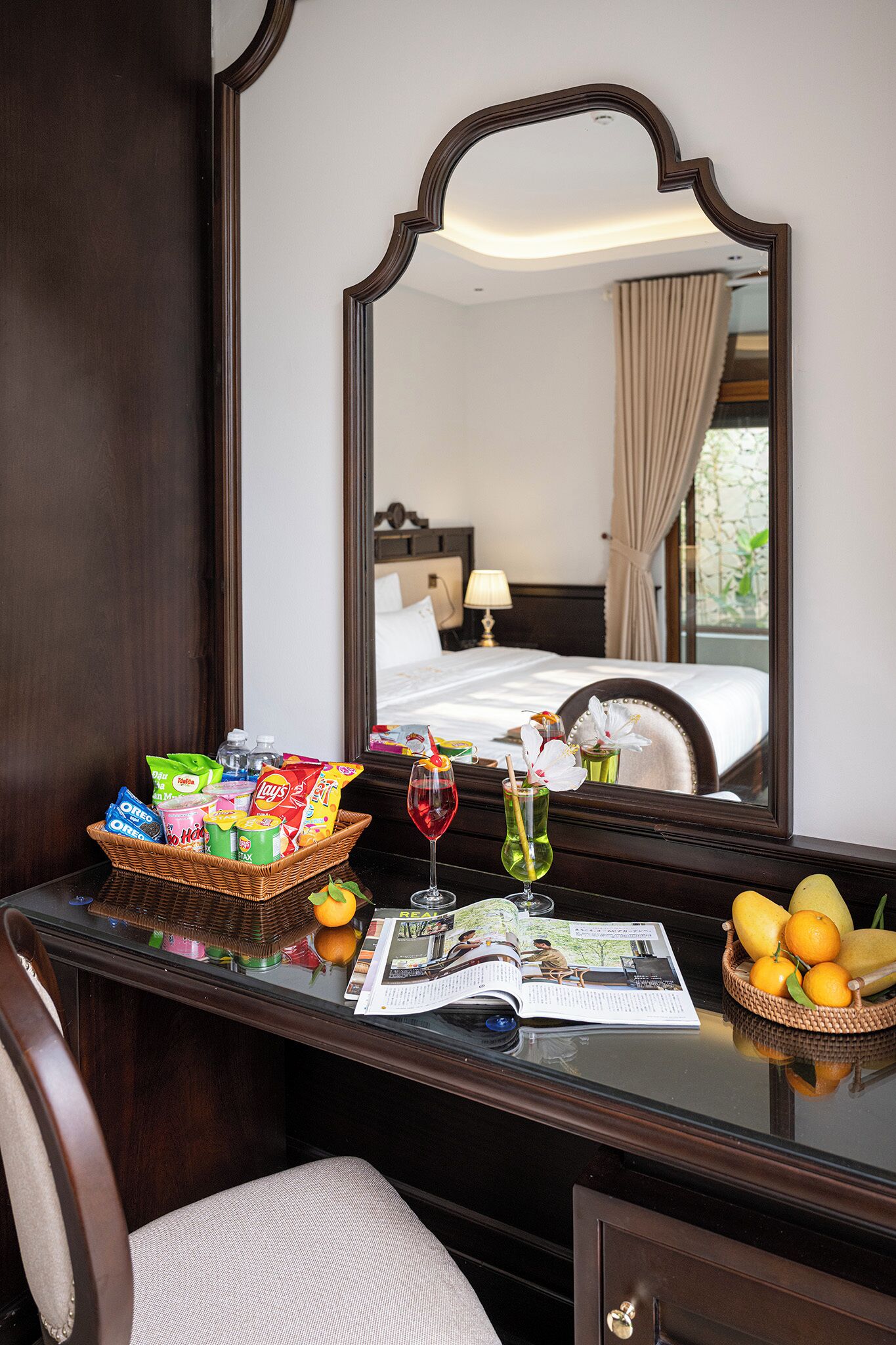 Habitación de hotel con una cama, una mesita de noche con aperitivos, una copa de vino tinto y una revista.