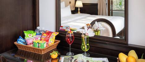 Habitación de hotel con una cama, una mesita de noche con aperitivos, una copa de vino tinto y una revista.