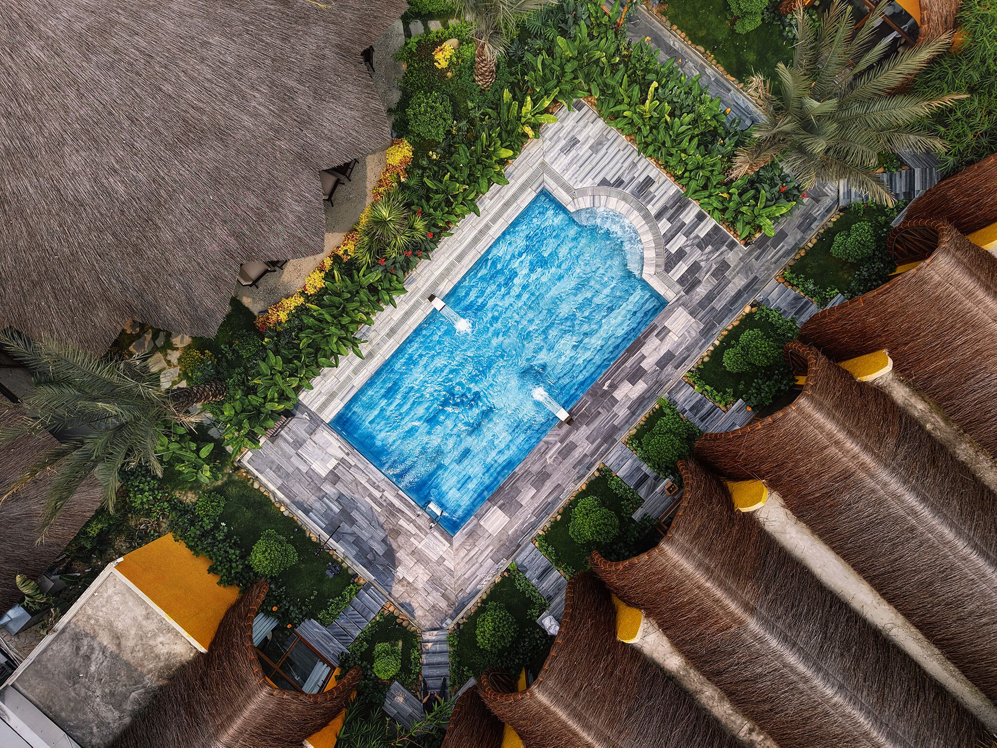Vista aérea de uma piscina rodeada por vegetação exuberante e uma estrutura com telhado de palha.
