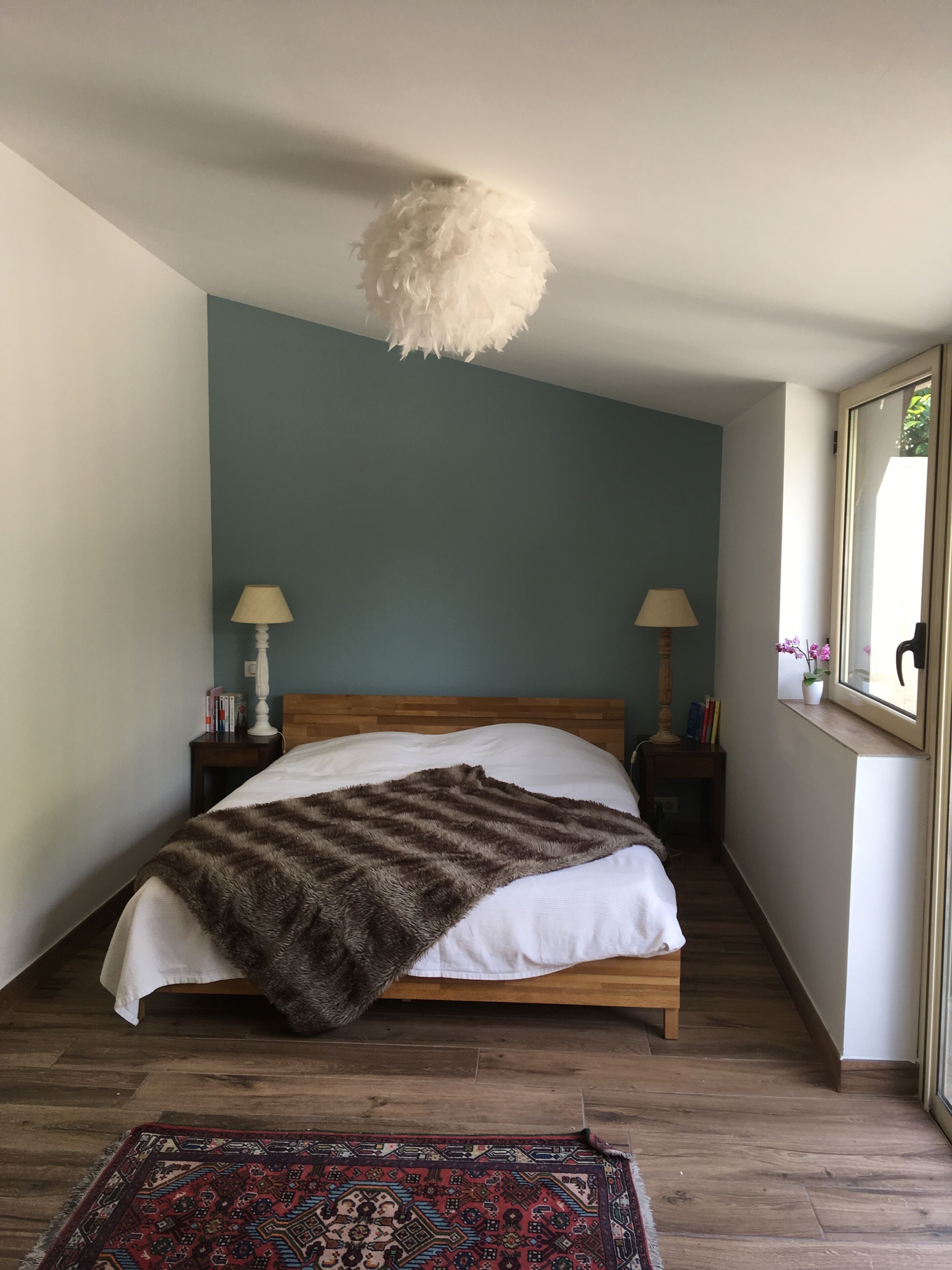 A bedroom with a bed, two bedside tables, a rug, and a hanging light fixture.