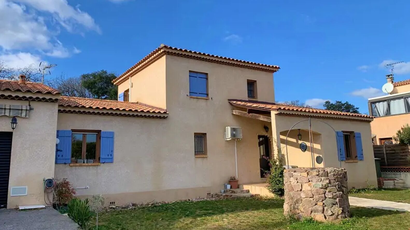 A two-story house with a stone wall in front, a tiled roof, and a small porch.