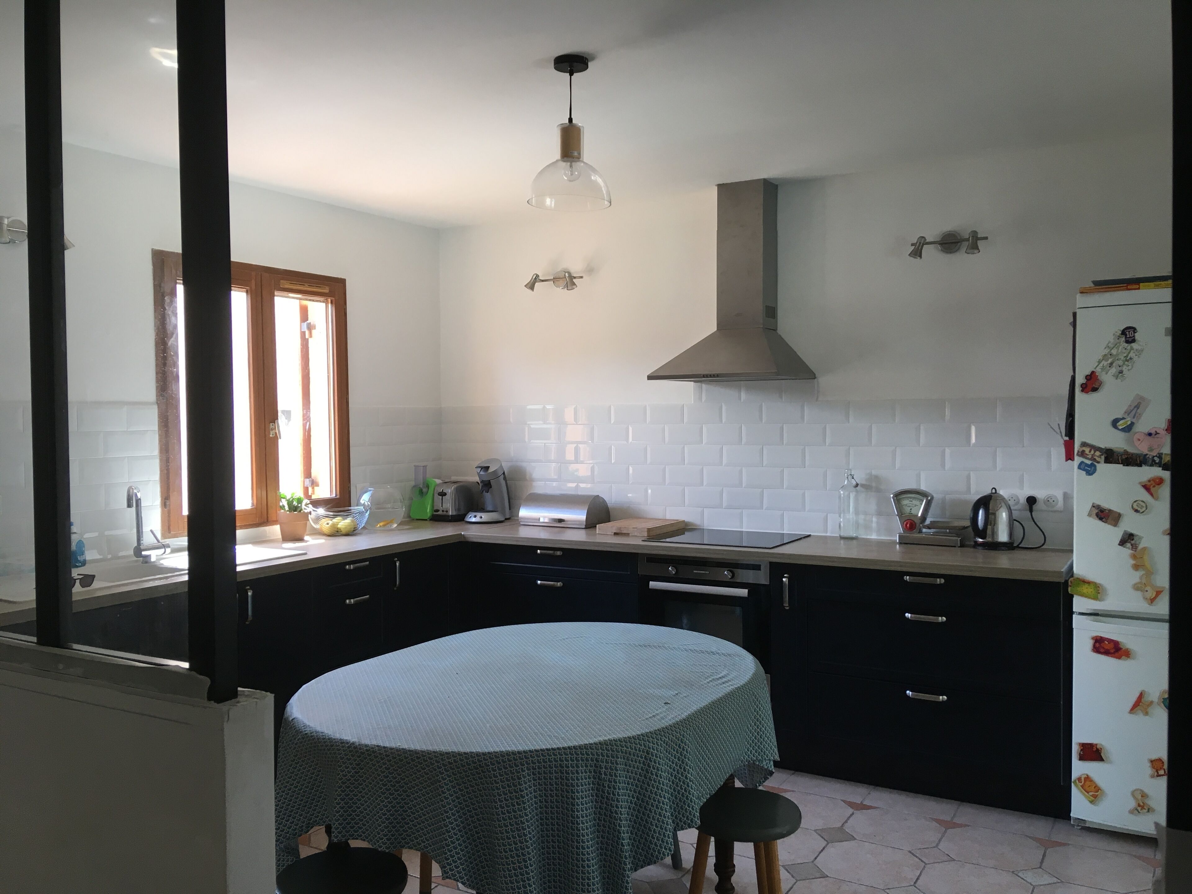 Een keuken met een ronde tafel, een hanglamp, een inbouwoven en een koelkast met magneten.