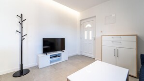 Een moderne woonkamer met een flatscreen televisie op een witte tv-meubel, een kapstok, een wit kastje en een houten garderobe.
