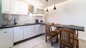 Een moderne keuken met witte kasten, een marmeren spatwand, een zwart aanrecht en een eethoek met houten stoelen.