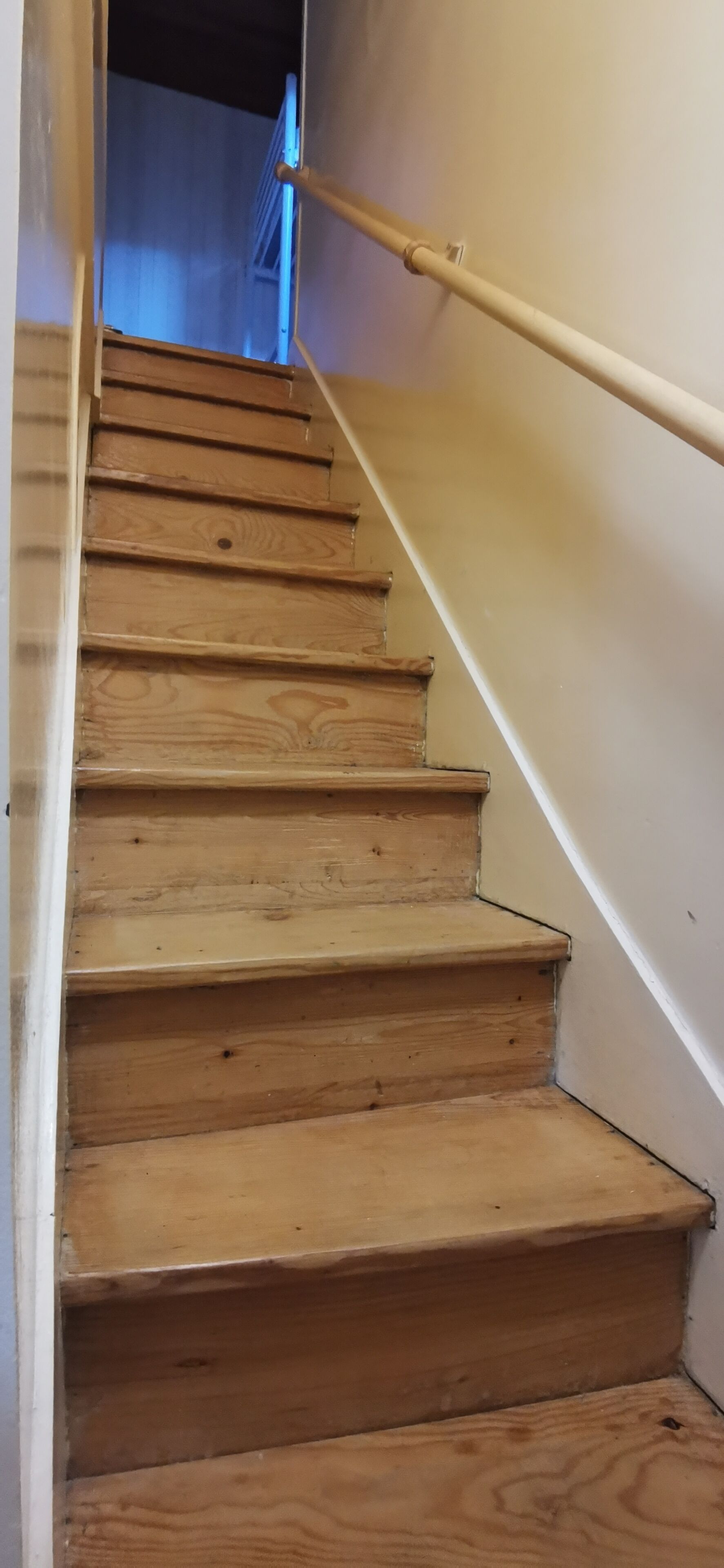 A wooden staircase with a handrail, leading to a room with a blue wall.
