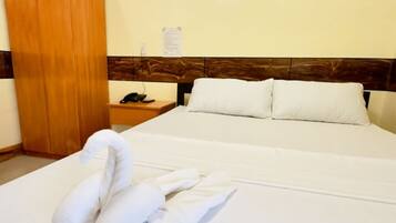 A hotel room with a bed, a wooden wardrobe, a nightstand with a phone, and a swan-shaped towel.