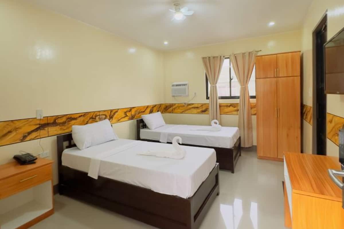 A hotel room with two beds, a desk, a wardrobe, and an air conditioning unit.