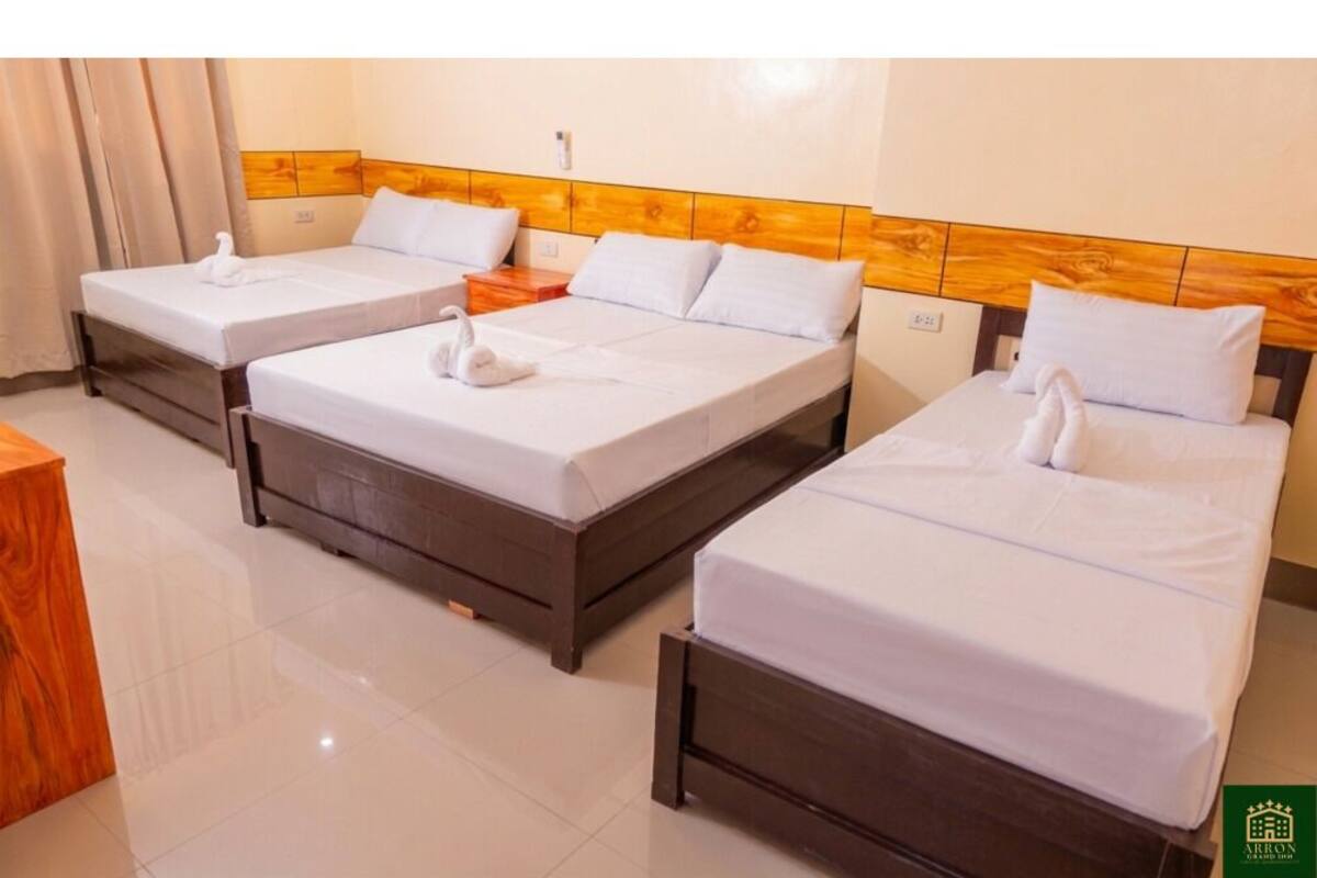 A hotel room with three beds, wooden headboards, white bedding, and a wooden nightstand.