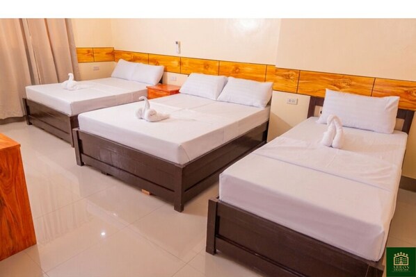 Una habitación de hotel con tres camas, cabeceros de madera, ropa de cama blanca y una mesita de noche de madera.